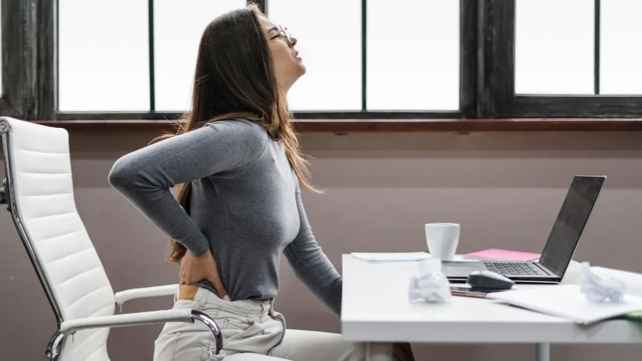 Mujer con dolor de espalda mientras trabaja en la oficina.